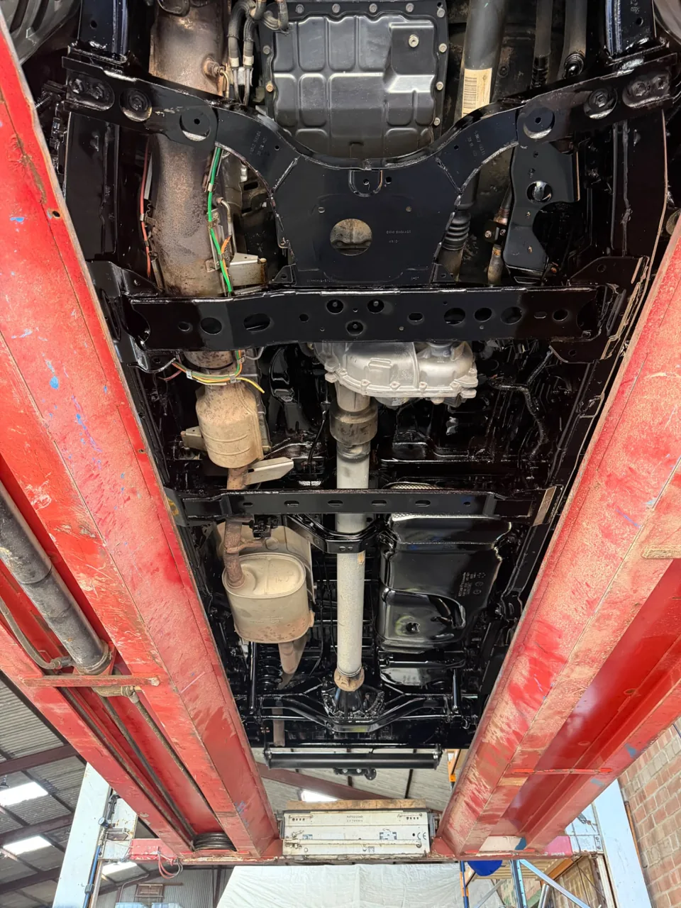 Vehicle chassis and drivetrain viewed from underneath on a workshop lift