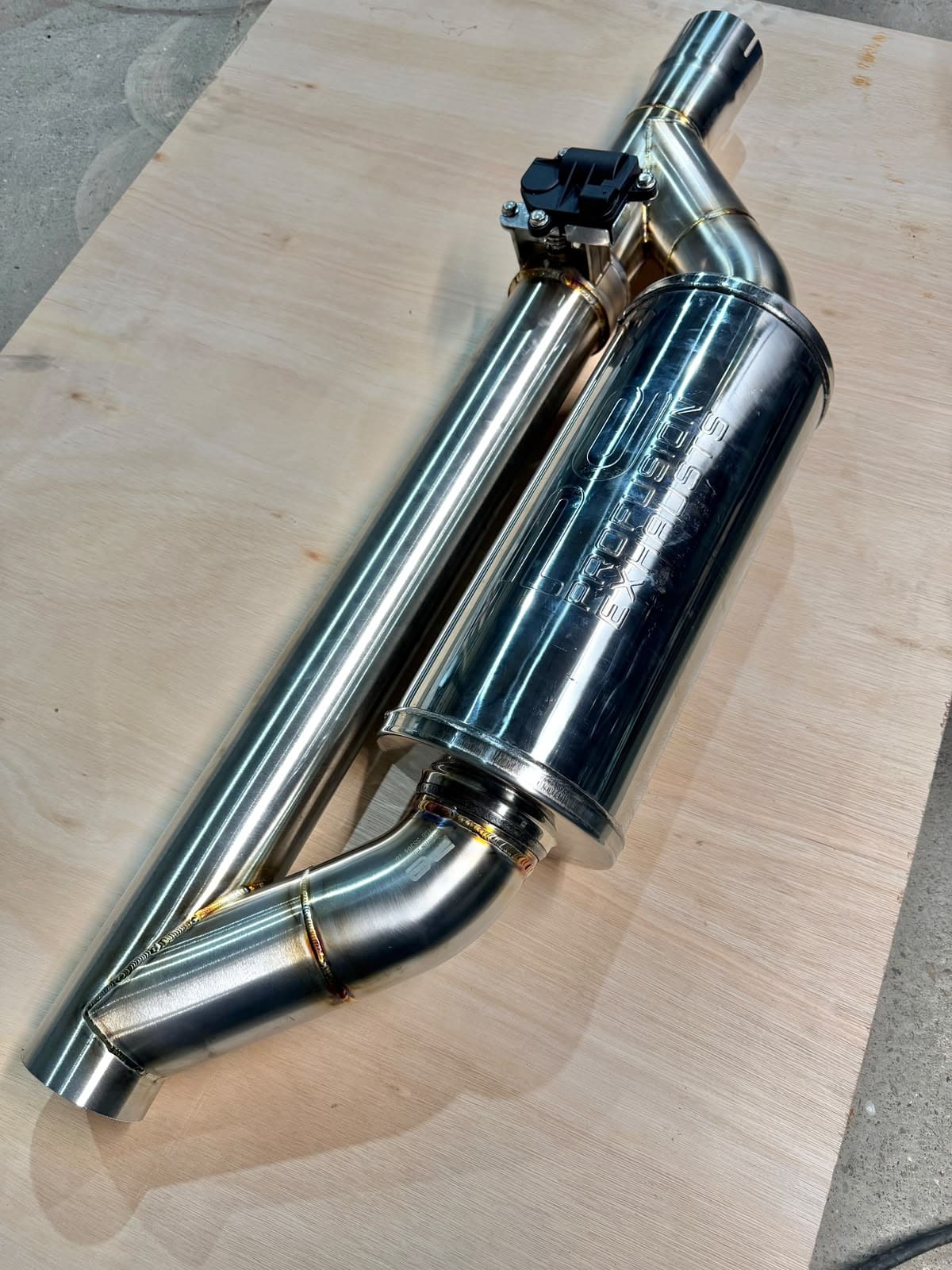 Manufactured stainless exhaust assembly with a silencer and valve on a wooden board