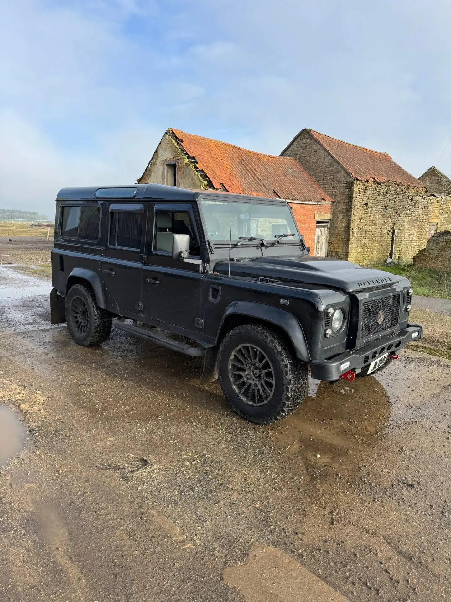 Black Land Rover Defender parked in a farmyard beside old brick barns