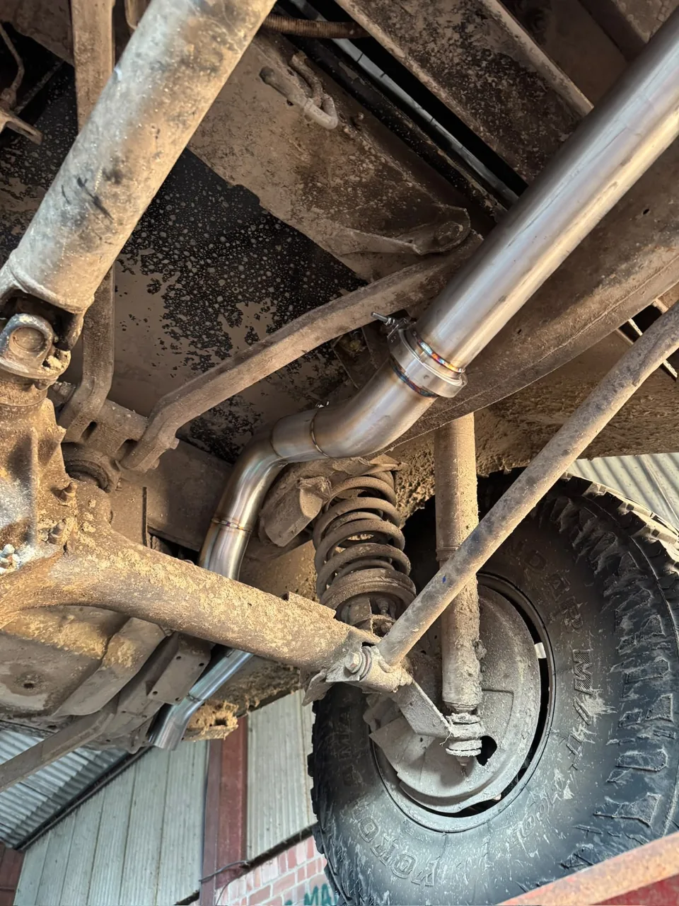 Stainless exhaust pipe beneath a vehicle beside its rear wheel and axle