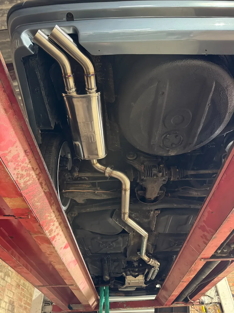 Vehicle underside on a lift showing stainless exhaust pipes and silencers