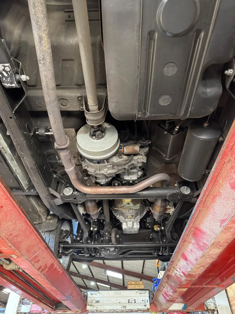 Vehicle underside on a lift showing drivetrain, fuel tank and exhaust routing