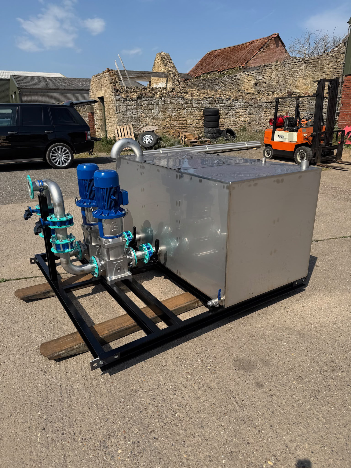 Stainless fabricated tank with blue pumps and connected pipework in the workshop yard