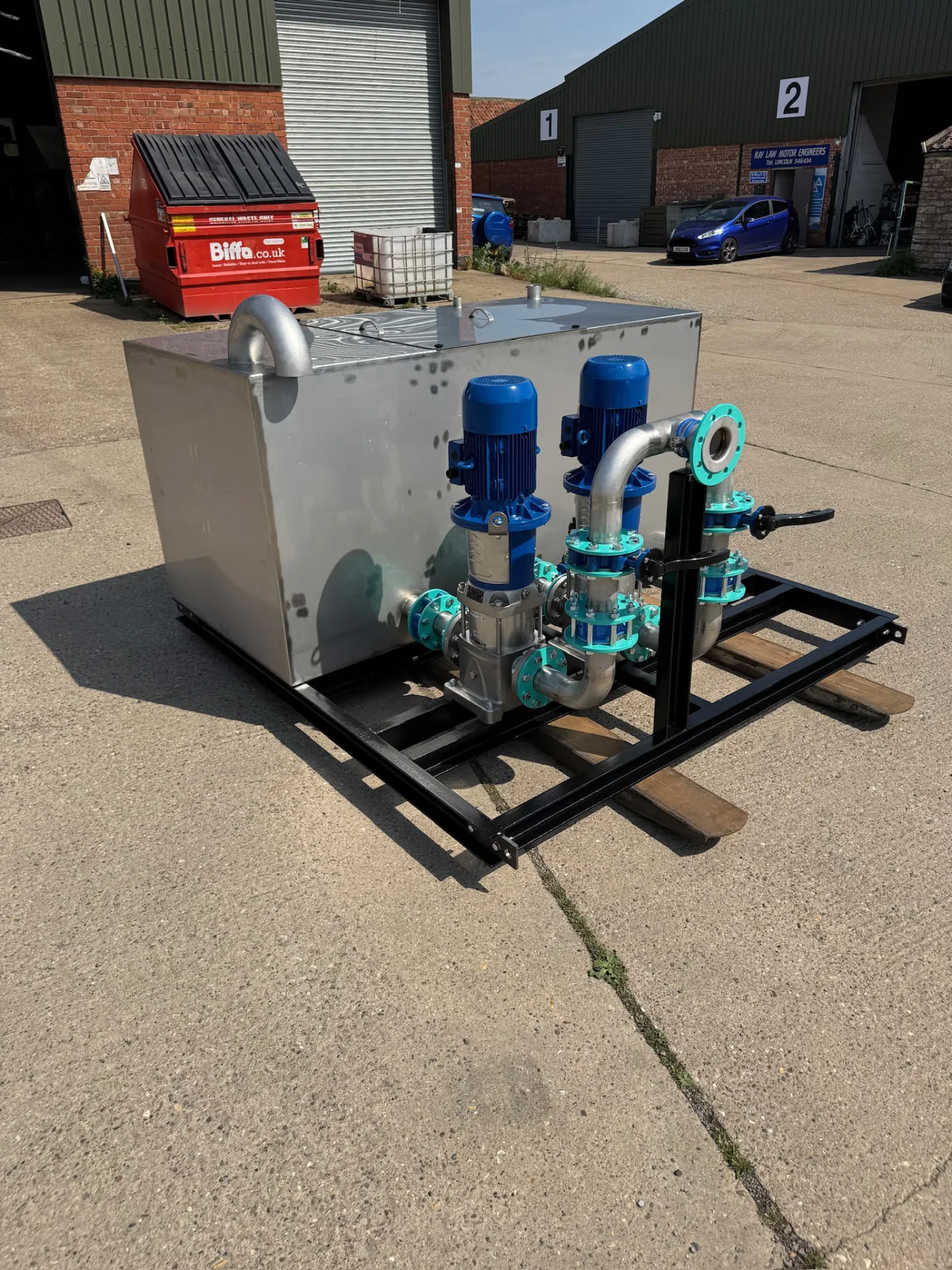 Stainless tank with blue pump and connected pipework on a black frame