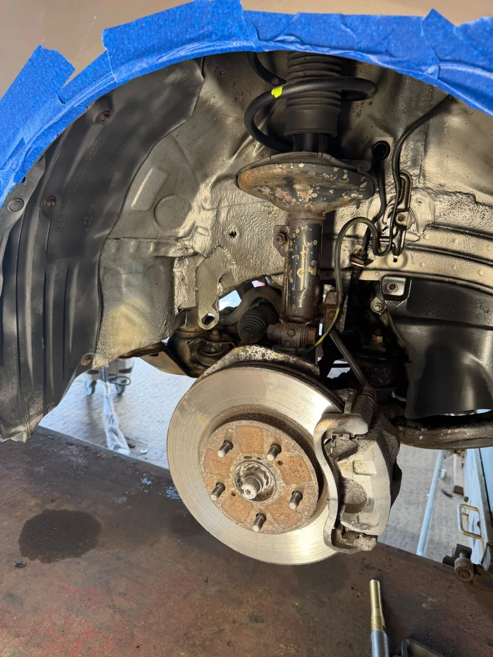 Vehicle wheel arch showing brake disc and corroded suspension parts