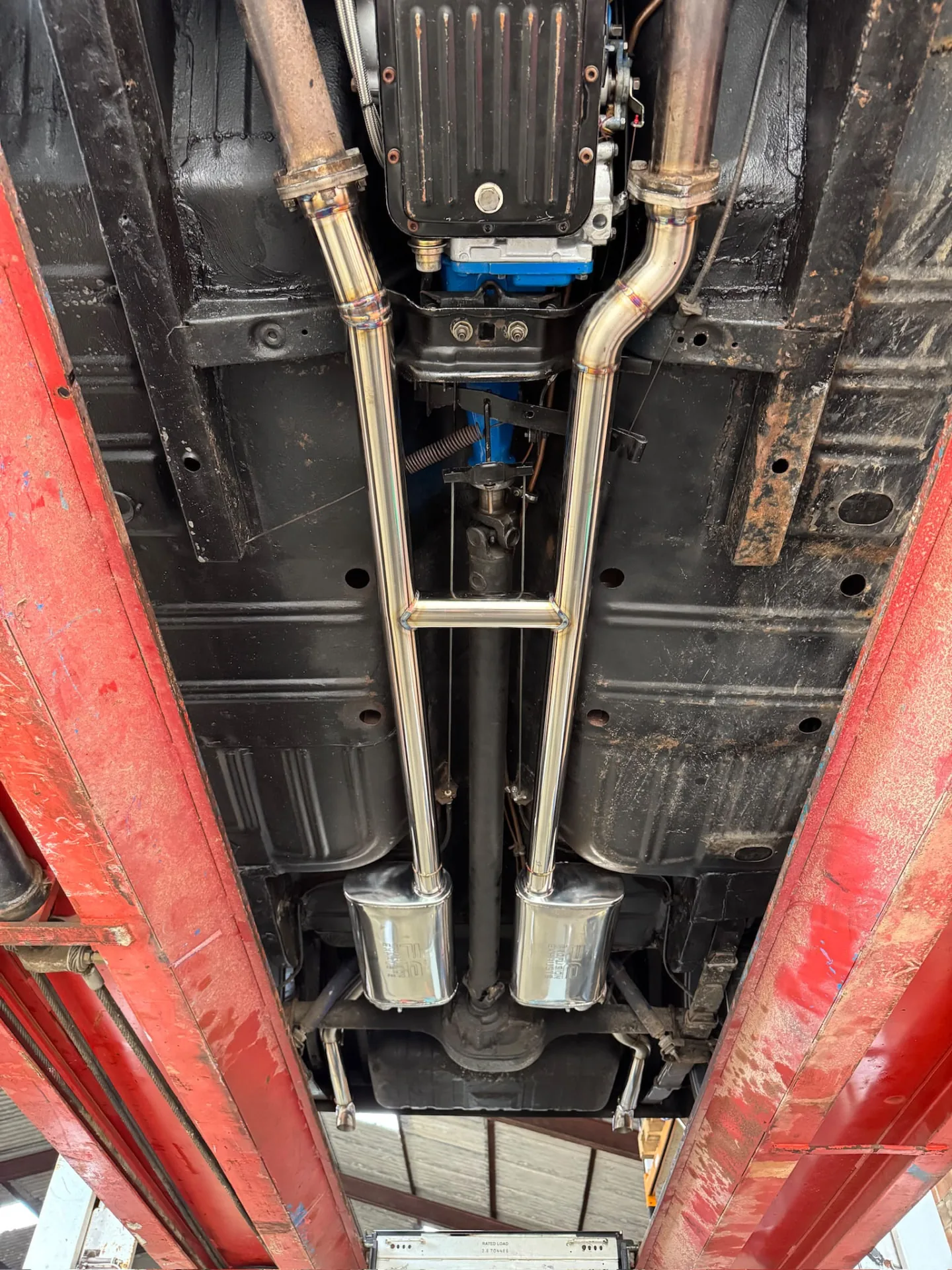 Twin stainless exhaust pipes running beneath a black vehicle underbody