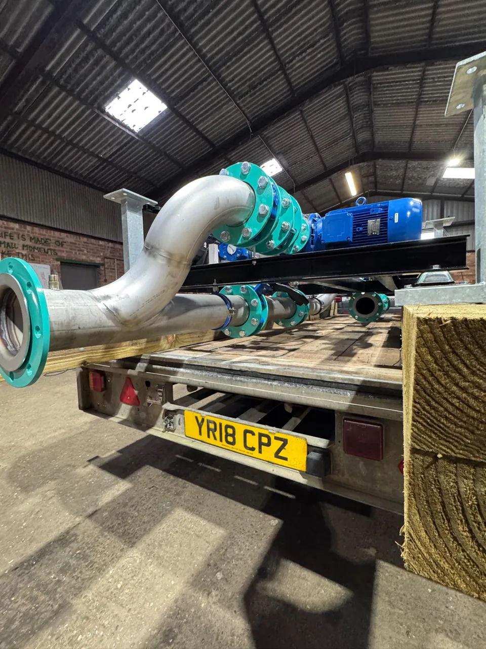 Large stainless pipe bends and blue industrial pump equipment on a truck
