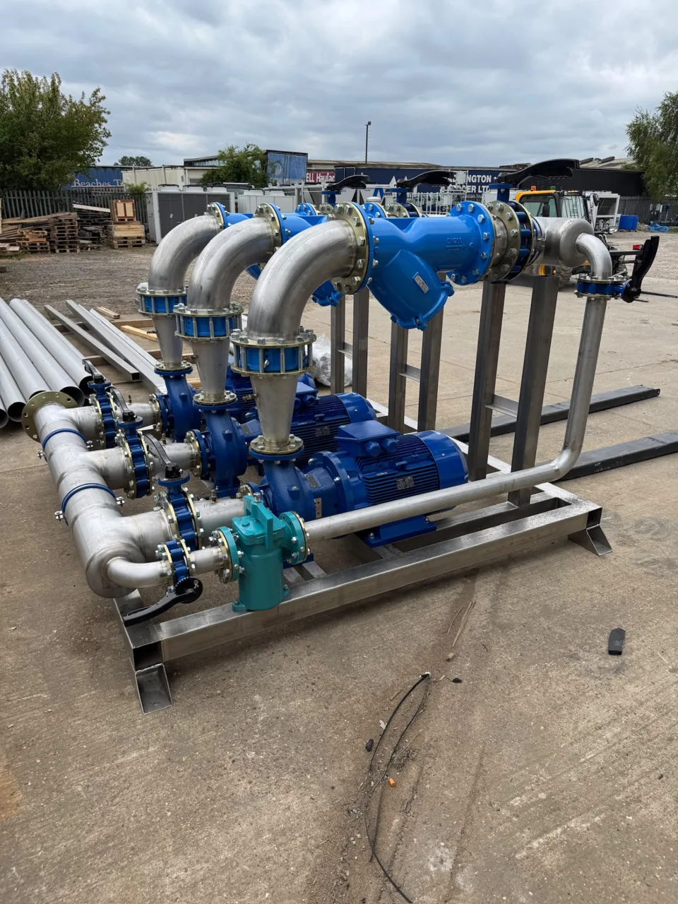 Fabricated stainless pipework and blue pump assembly on a skid outdoors