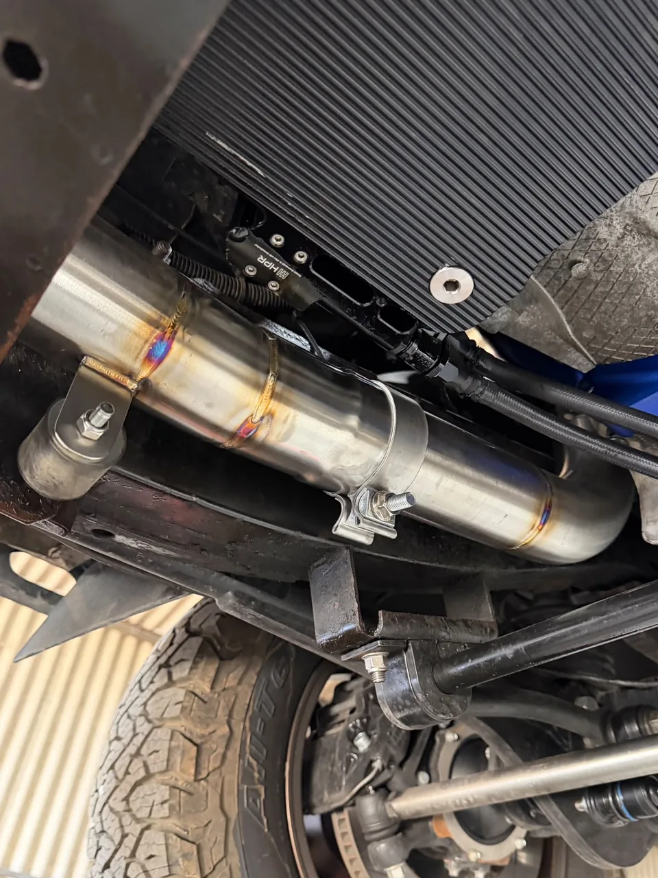 Custom stainless exhaust fitted beneath a vehicle beside a cooling unit