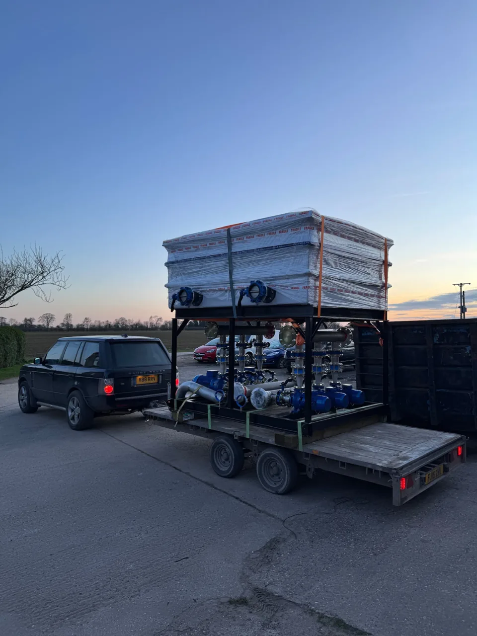 Stainless tank and pipework skid carried on a trailer at dusk