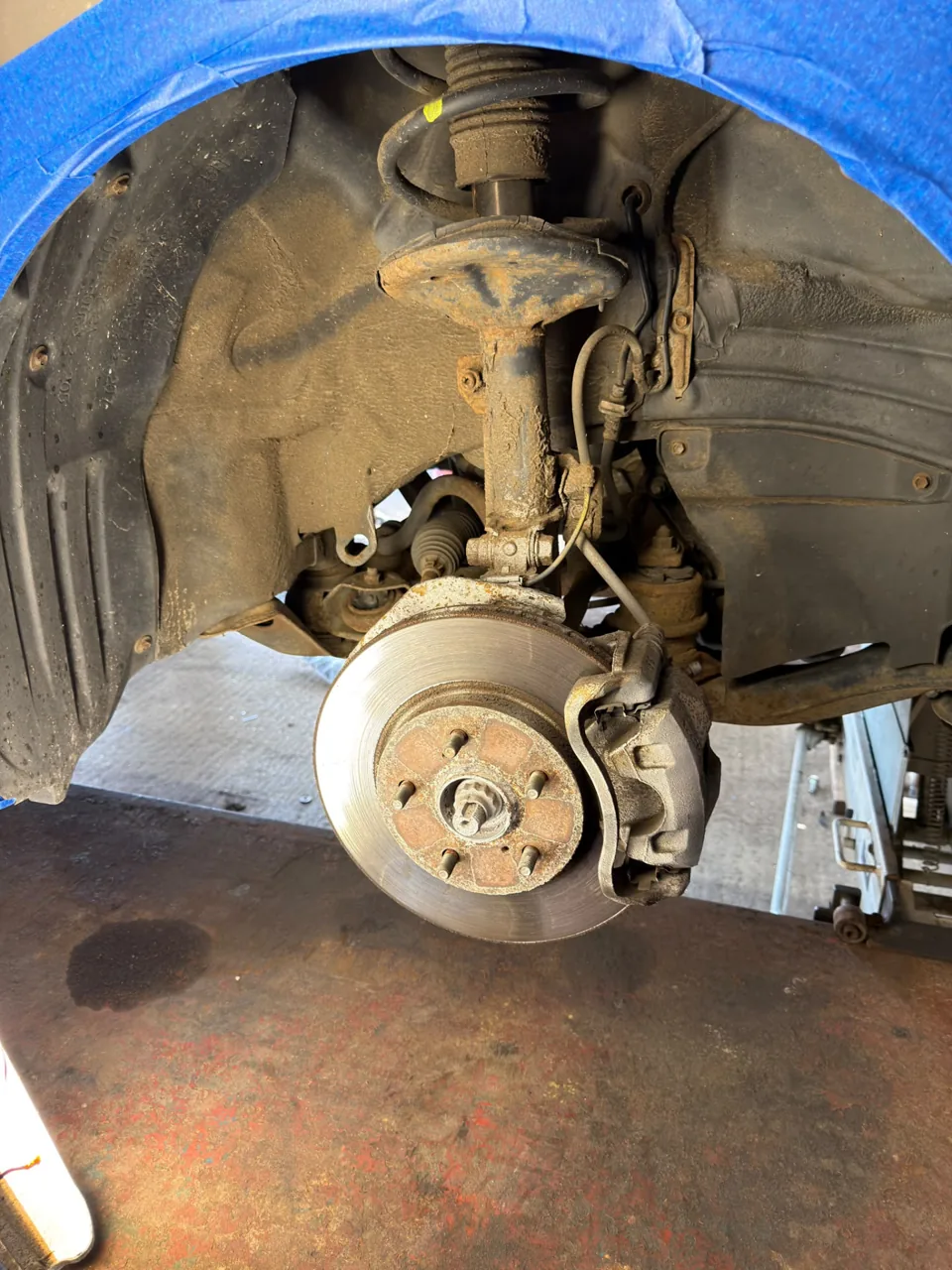 Vehicle wheel arch with exposed brake disc and surface corrosion on suspension parts