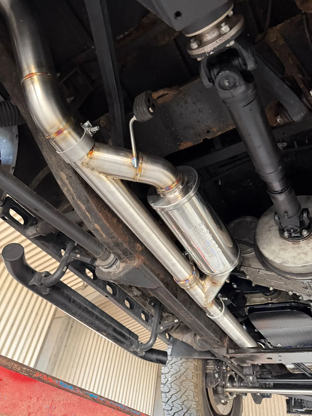 Custom stainless exhaust installed beneath a vehicle beside the rear axle